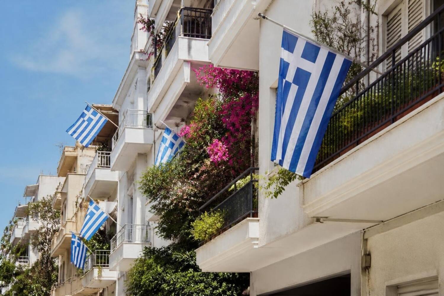 Griechische Flaggen an den Balkonen eines Wohnhauses in Athen mit blühender Bougainvillea